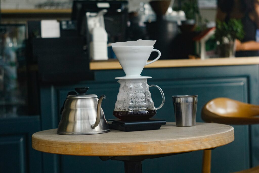 Inviting café scene showing a pour-over coffee setup with a kettle and metal cup on a wooden table.