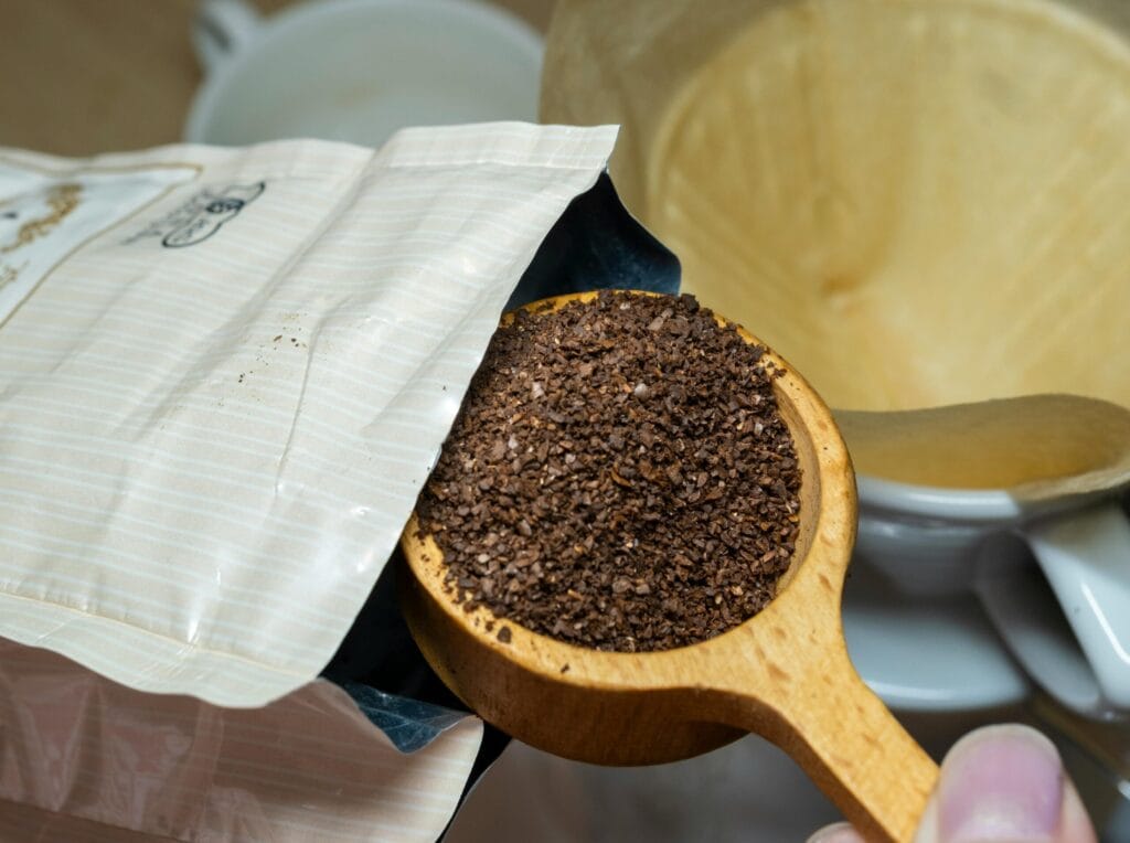 Resep V60 Juara Dunia: Rahasia "4:6 Method" Tetsu Kasuya Wooden scoop with fresh coffee grounds being poured into a drip filter, ready for brewing.
