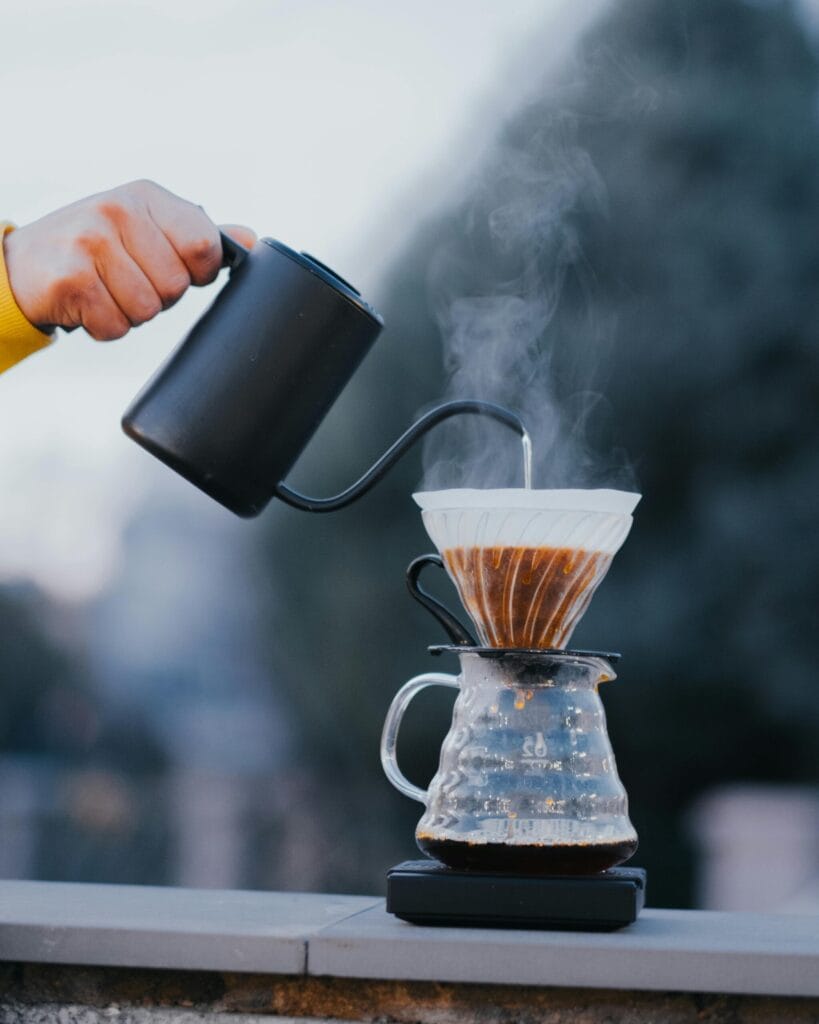 Outdoor coffee brewing with a V60 dripper and black kettle, showcasing boiling water process.